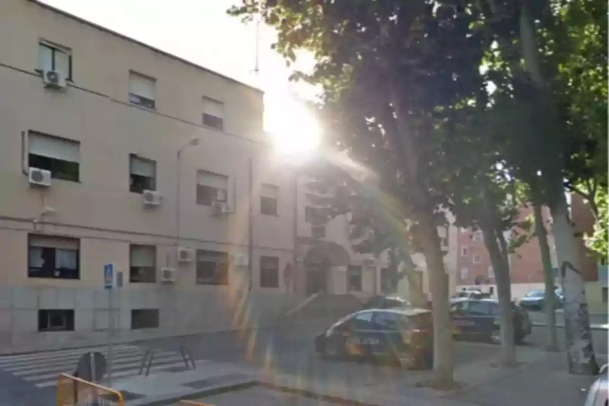 Edificio con ventanas y unidades de aire acondicionado, rodeado de árboles y coches estacionados, con el sol brillando intensamente desde el fondo. Edificio con ventanas y unidades de aire acondicionado, rodeado de árboles y coches estacionados, con el sol brillando intensamente desde el fondo.