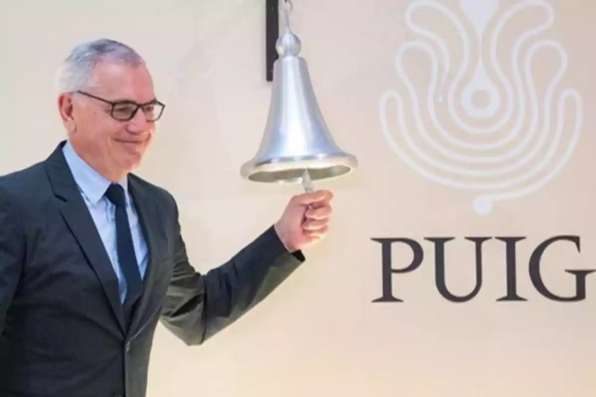 Un hombre de traje y corbata toca una campana junto a un logotipo que dice 