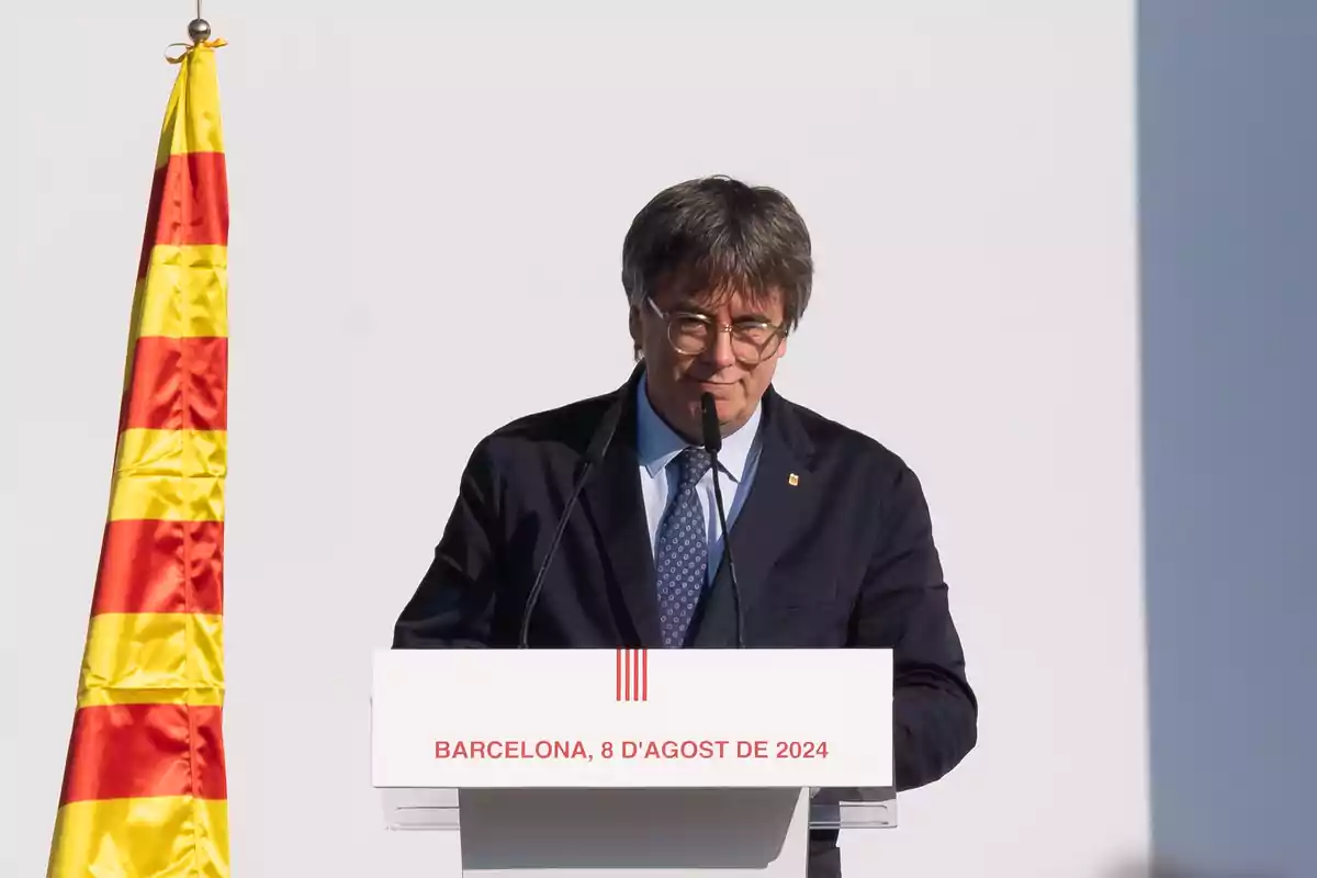 Hombre dando un discurso en un podio con una bandera catalana a su lado.