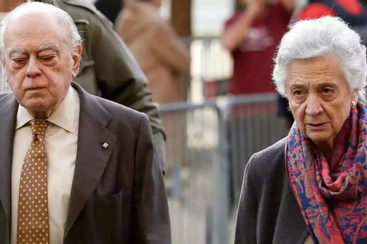 Dos personas mayores caminando juntas, el hombre lleva traje y corbata y la mujer lleva un abrigo y una bufanda colorida.