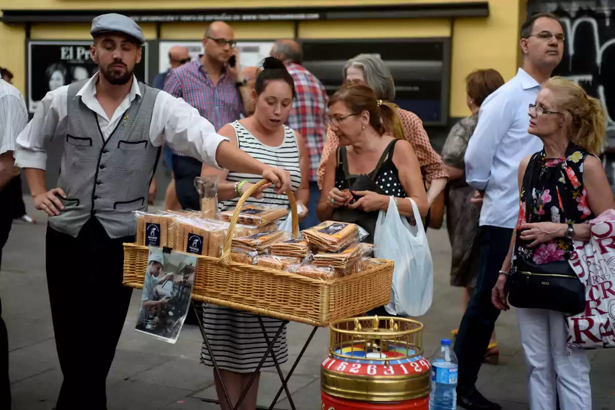 Un vendedor ambulante ofrece productos de panadería a un grupo de personas en una calle concurrida.