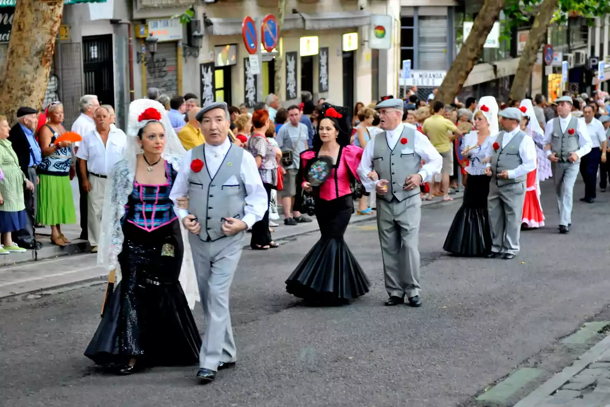 Personas vestidas con trajes tradicionales desfilan por una calle mientras una multitud observa.