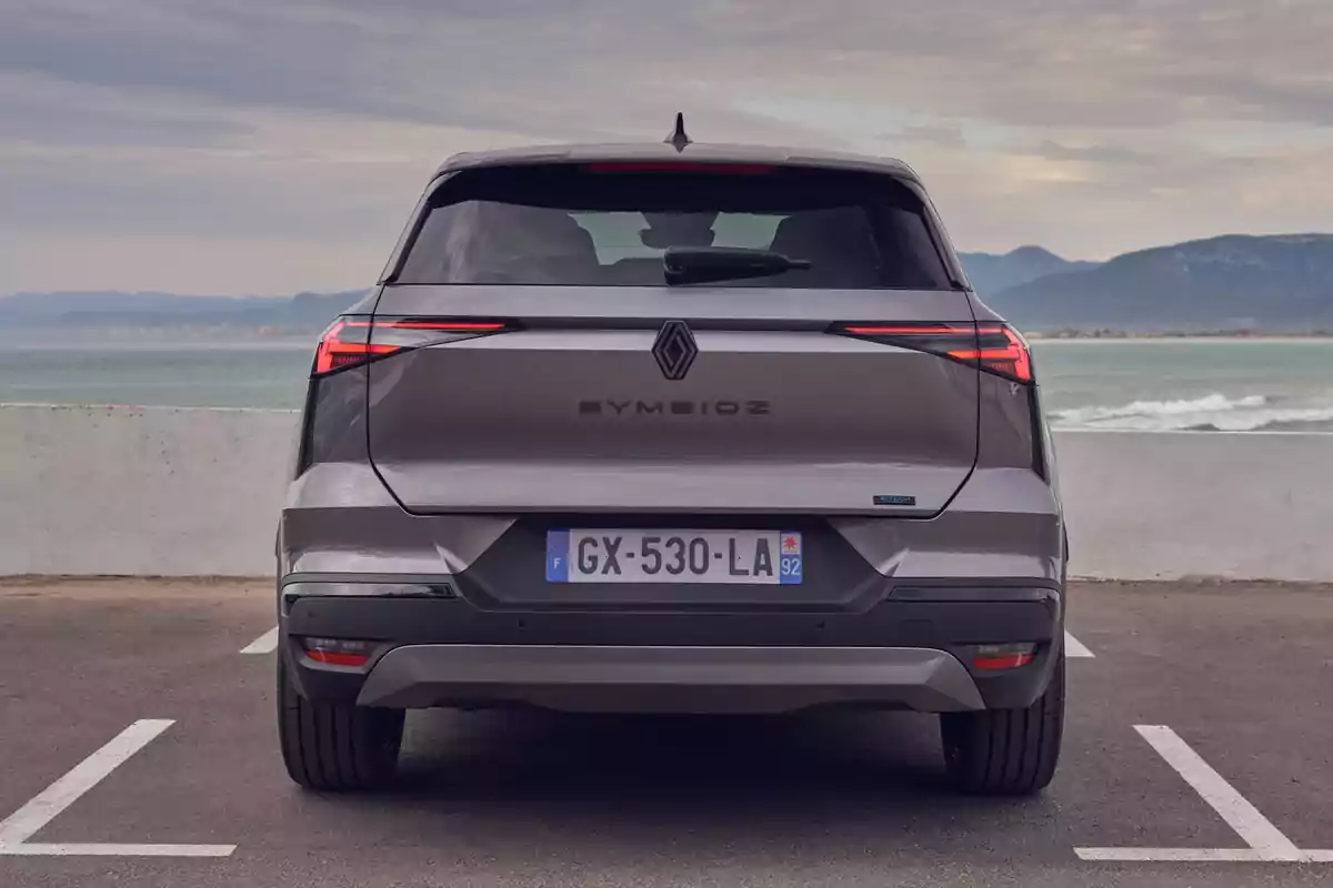 Un Renault Symbioz Hybrid gris estacionado en un aparcamiento frente al mar con montañas al fondo. Un Renault Symbioz Hybrid gris estacionado en un aparcamiento frente al mar con montañas al fondo.