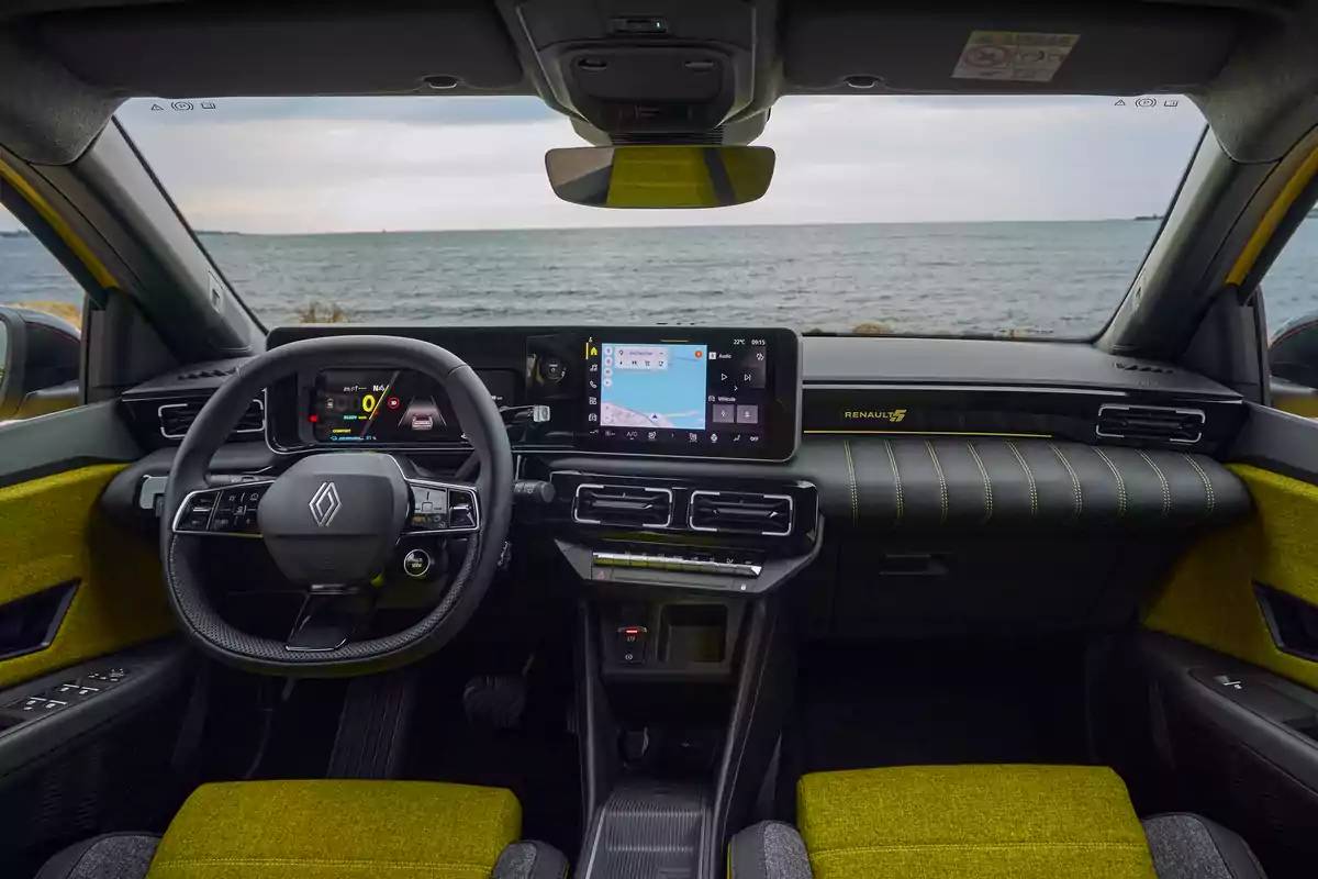 Interior de un automóvil Renault 5 con vista al mar a través del parabrisas, mostrando un volante moderno y una pantalla de navegación en el tablero.