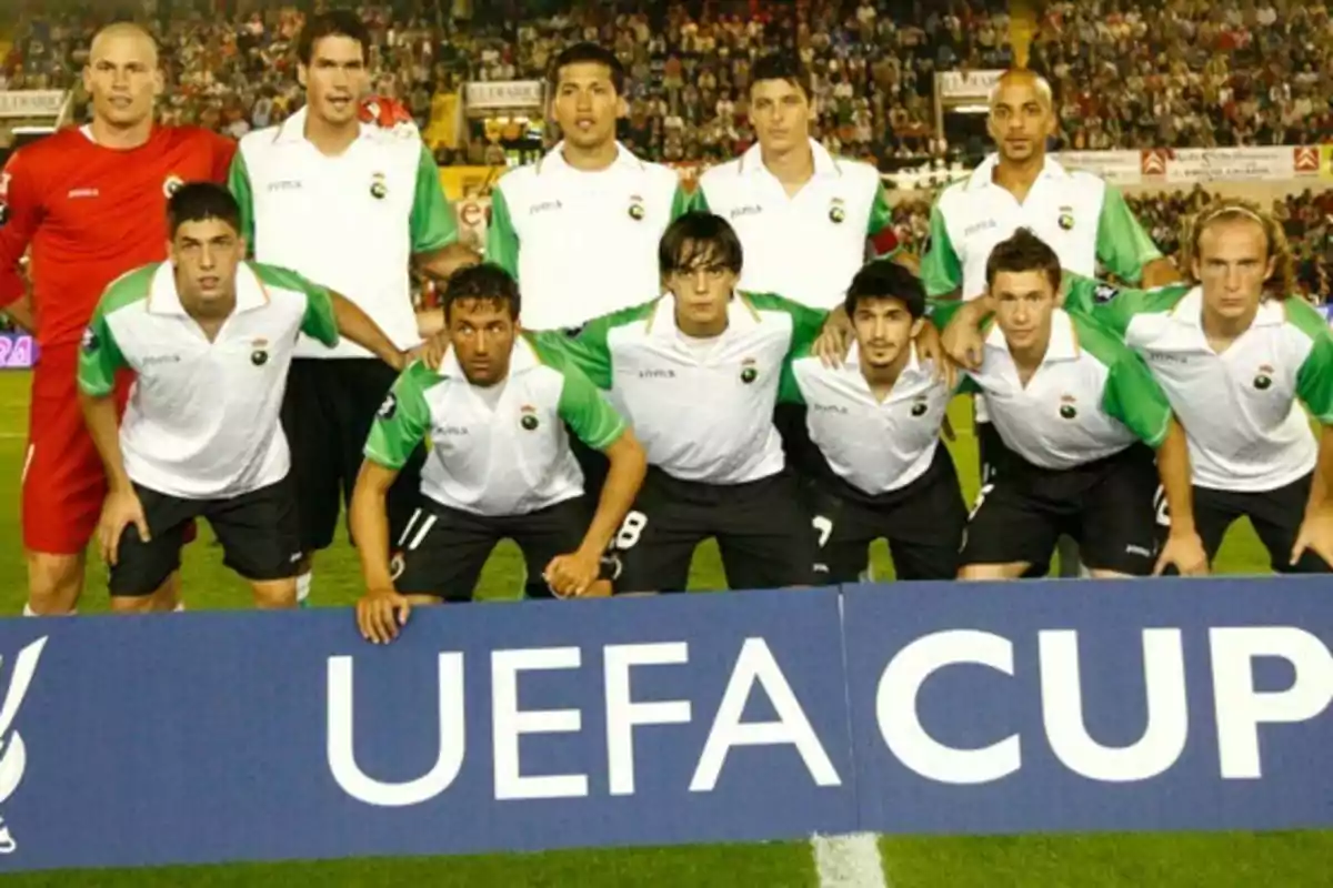 Un equipo de fútbol posando para una foto grupal antes de un partido de la UEFA Cup, con jugadores vistiendo uniformes blancos y verdes y un estadio lleno de espectadores al fondo.