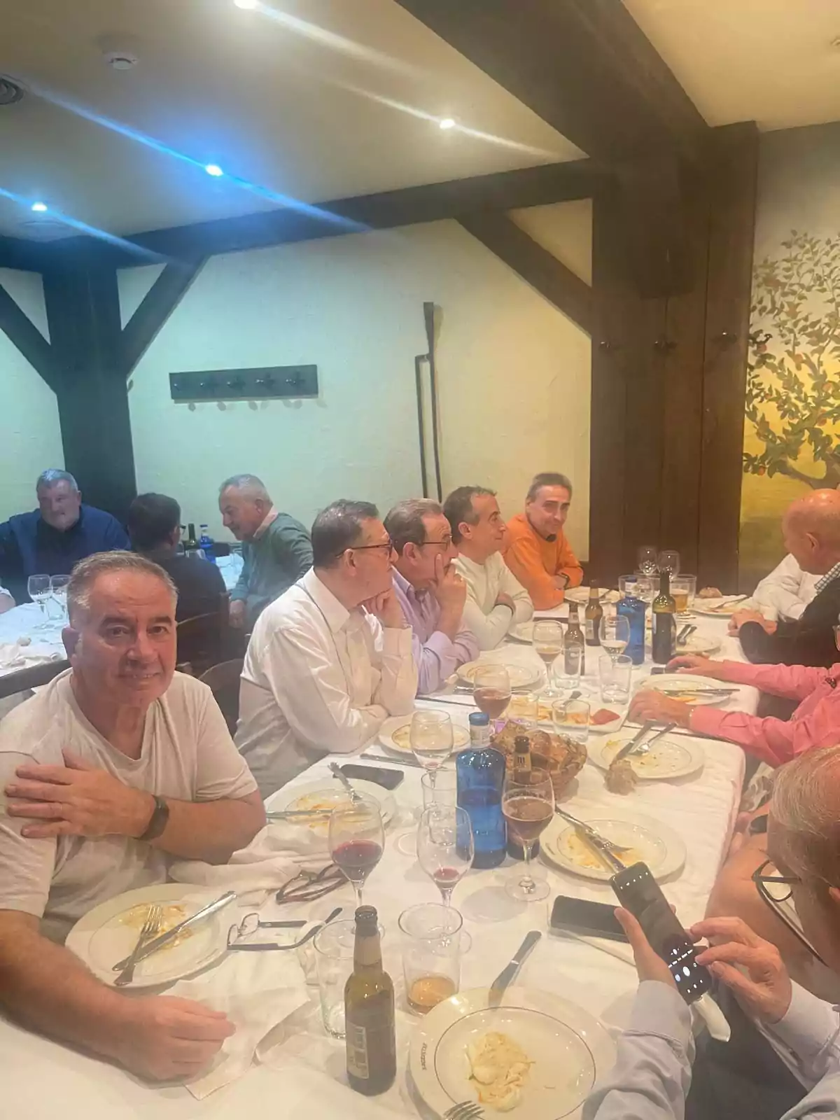 Un grupo de personas sentadas alrededor de una mesa en un restaurante, con platos y copas de vino sobre la mesa.