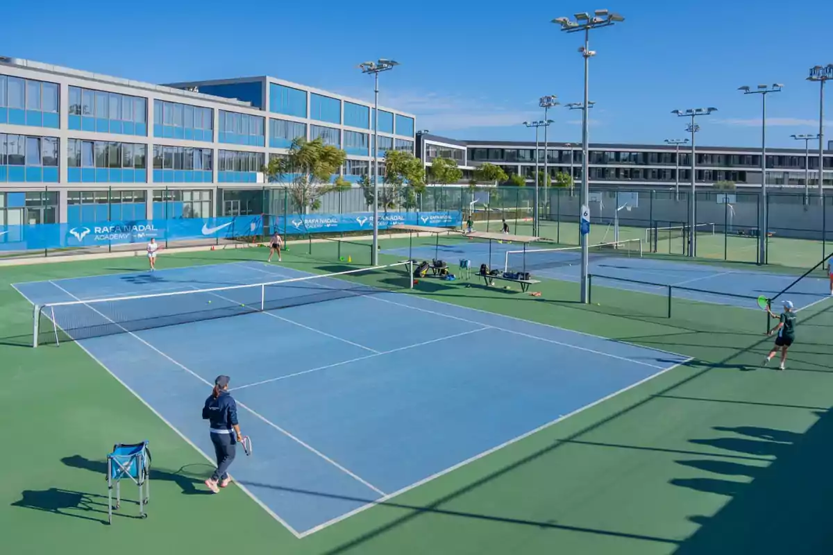 Personas jugando al tenis en una cancha al aire libre con un edificio moderno al fondo.