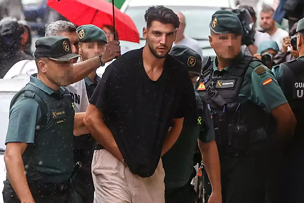 Un hombre escoltado por varios agentes de la Guardia Civil bajo la lluvia.