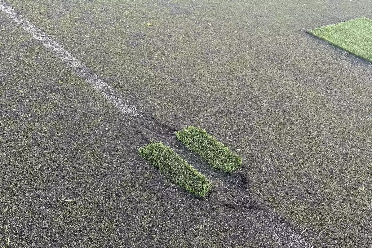 Campo de césped artificial con una línea blanca y dos parches de césped levantados.