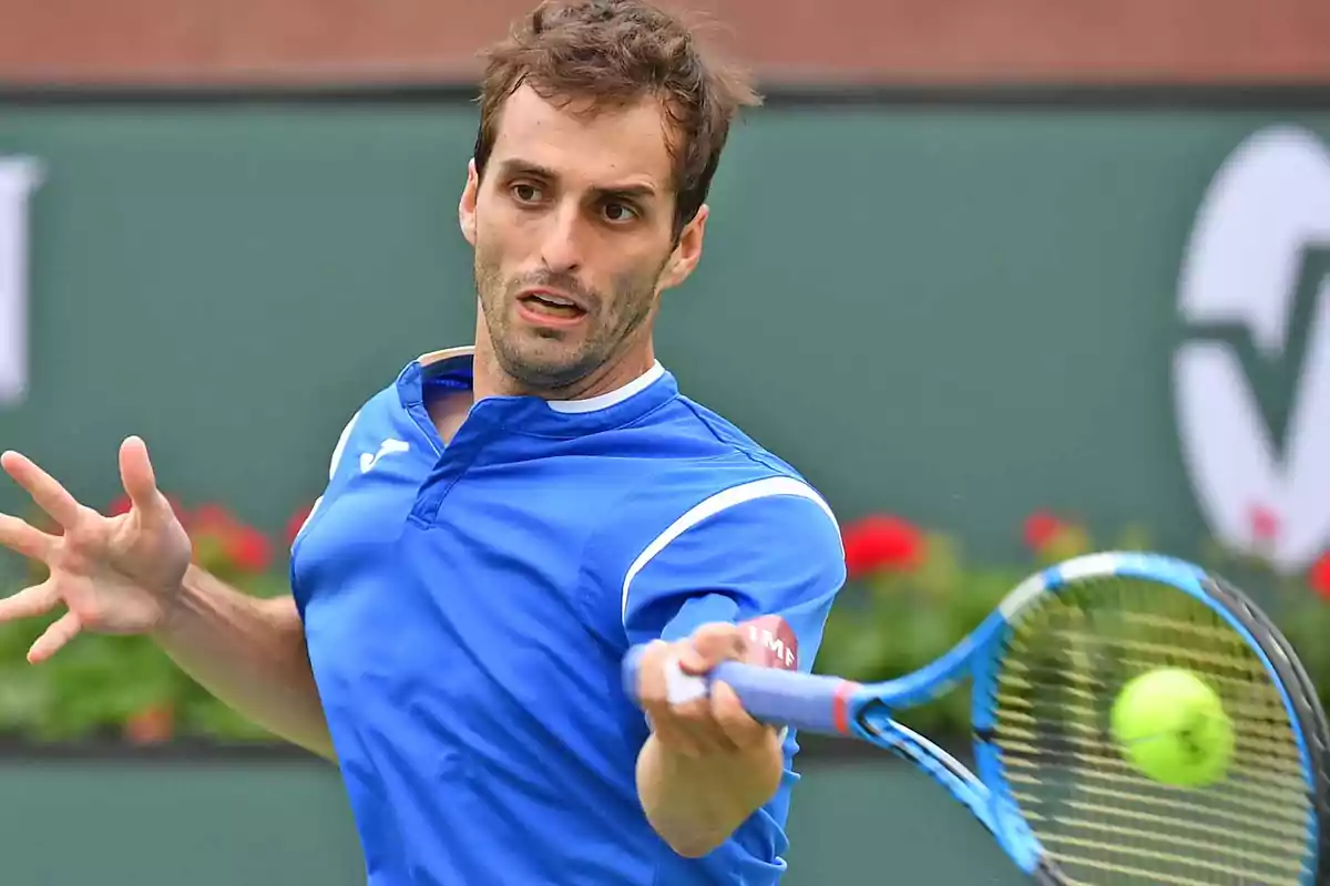 Un tenista en acción durante un partido con una raqueta azul y una pelota de tenis en movimiento. Un tenista en acción durante un partido con una raqueta azul y una pelota de tenis en movimiento.