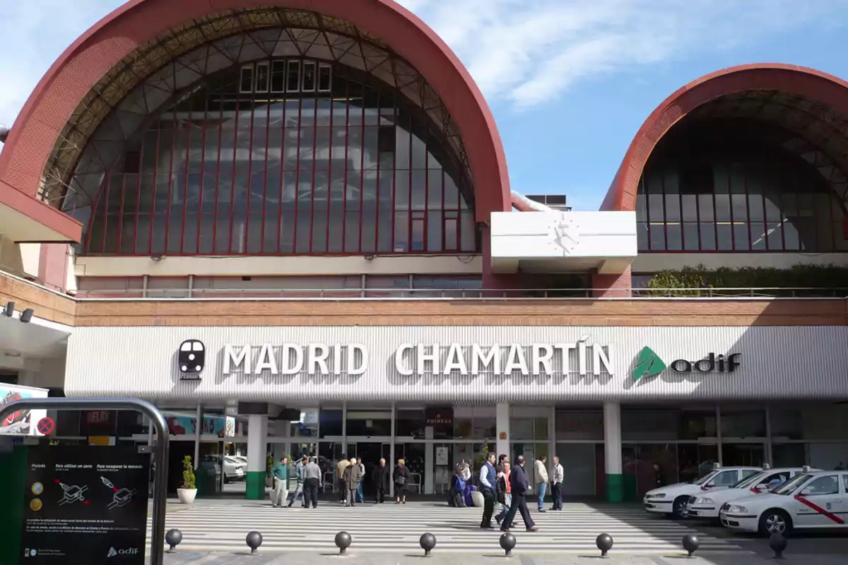 Fachada de la estación de tren Madrid Chamartín con personas caminando y taxis estacionados.