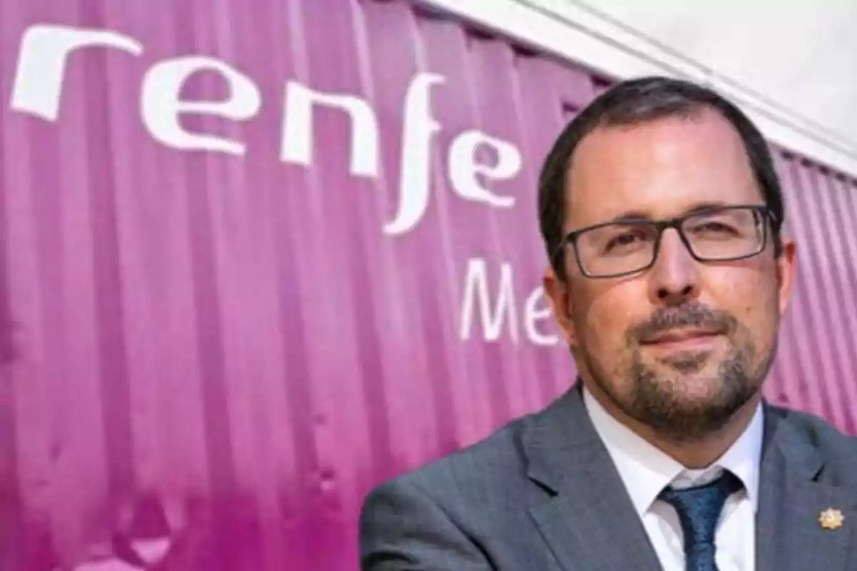 Un hombre con gafas y traje está frente a un contenedor morado con el logo de Renfe.