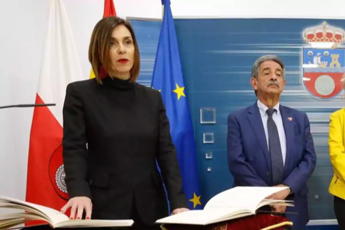 Una mujer y un hombre de pie en una ceremonia oficial con banderas y un libro abierto frente a ellos. Una mujer y un hombre de pie en una ceremonia oficial con banderas y un libro abierto frente a ellos.