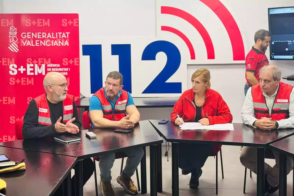 Un grupo de personas con chalecos rojos se encuentra reunido en una sala de emergencias de la Generalitat Valenciana, con un cartel de 