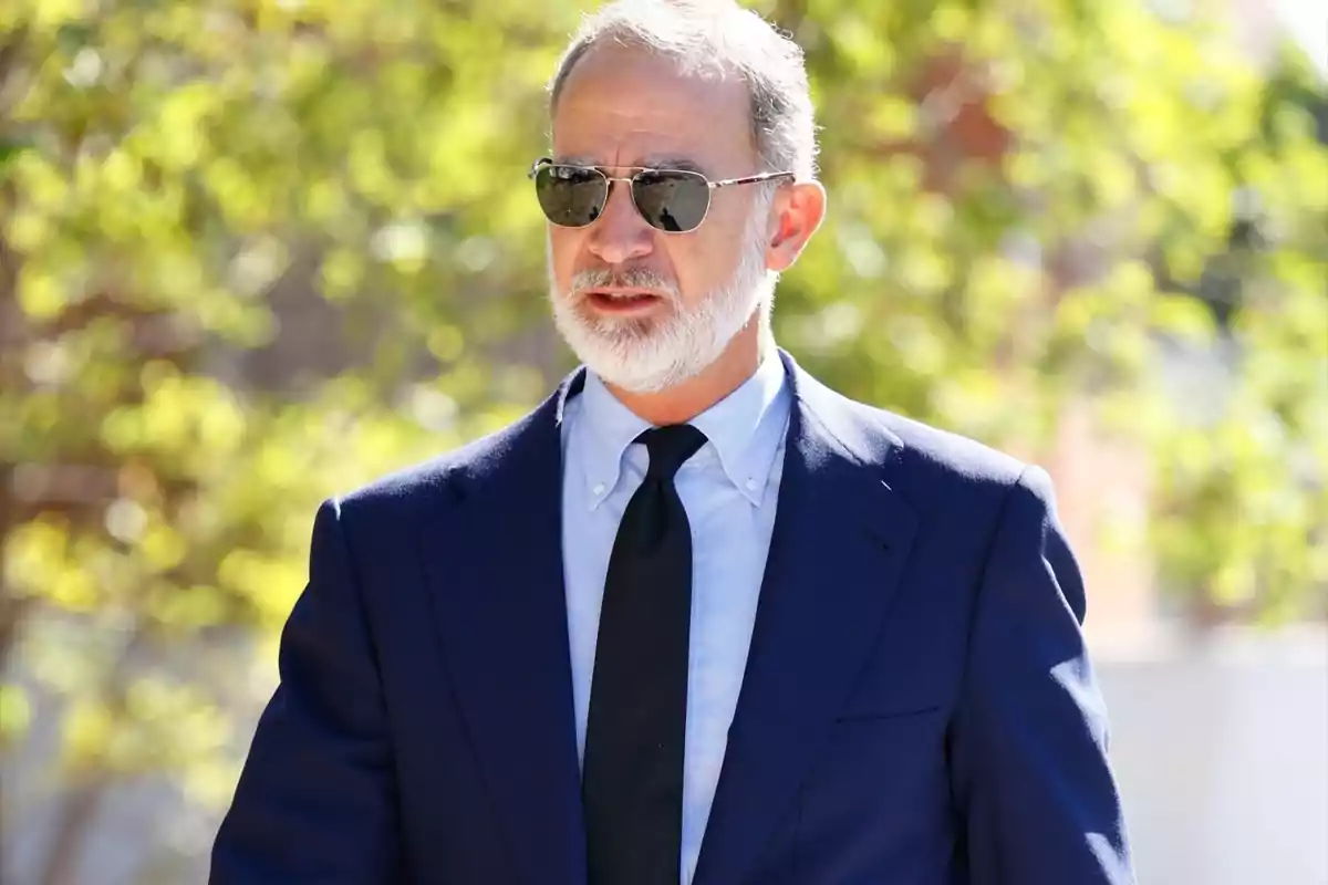 El rey Felipe VI, con traje azul marino, corbata negra y gafas de sol, luce semblante serio acudiendo al último adiós de Juan Gómez-Acebo