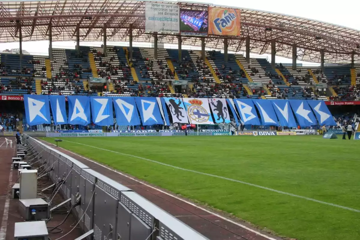 Un estadio de fútbol con gradas parcialmente llenas y una gran pancarta azul que dice 