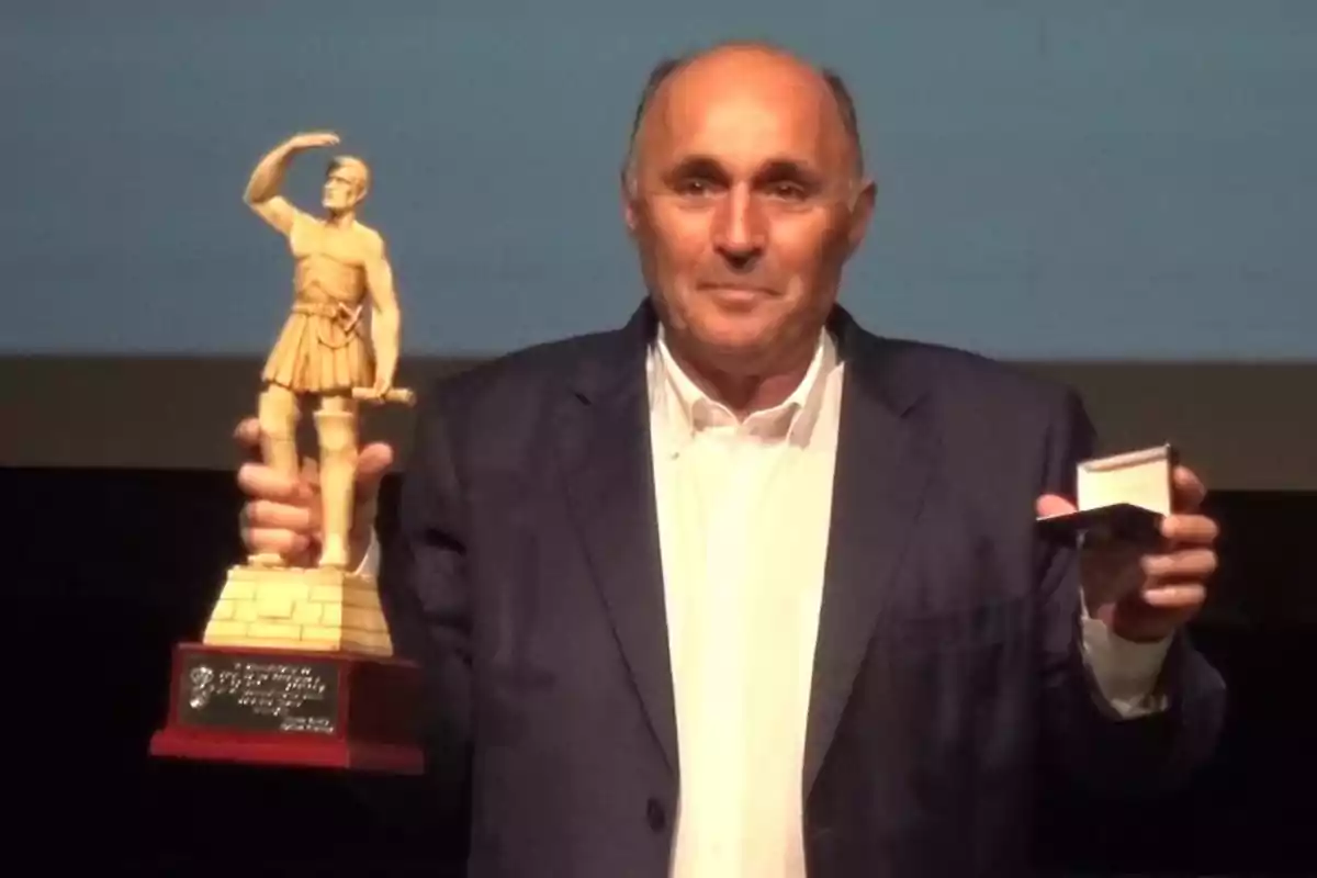 Un hombre sostiene un trofeo con una figura de un guerrero y una caja pequeña en sus manos. Un hombre sostiene un trofeo con una figura de un guerrero y una caja pequeña en sus manos.