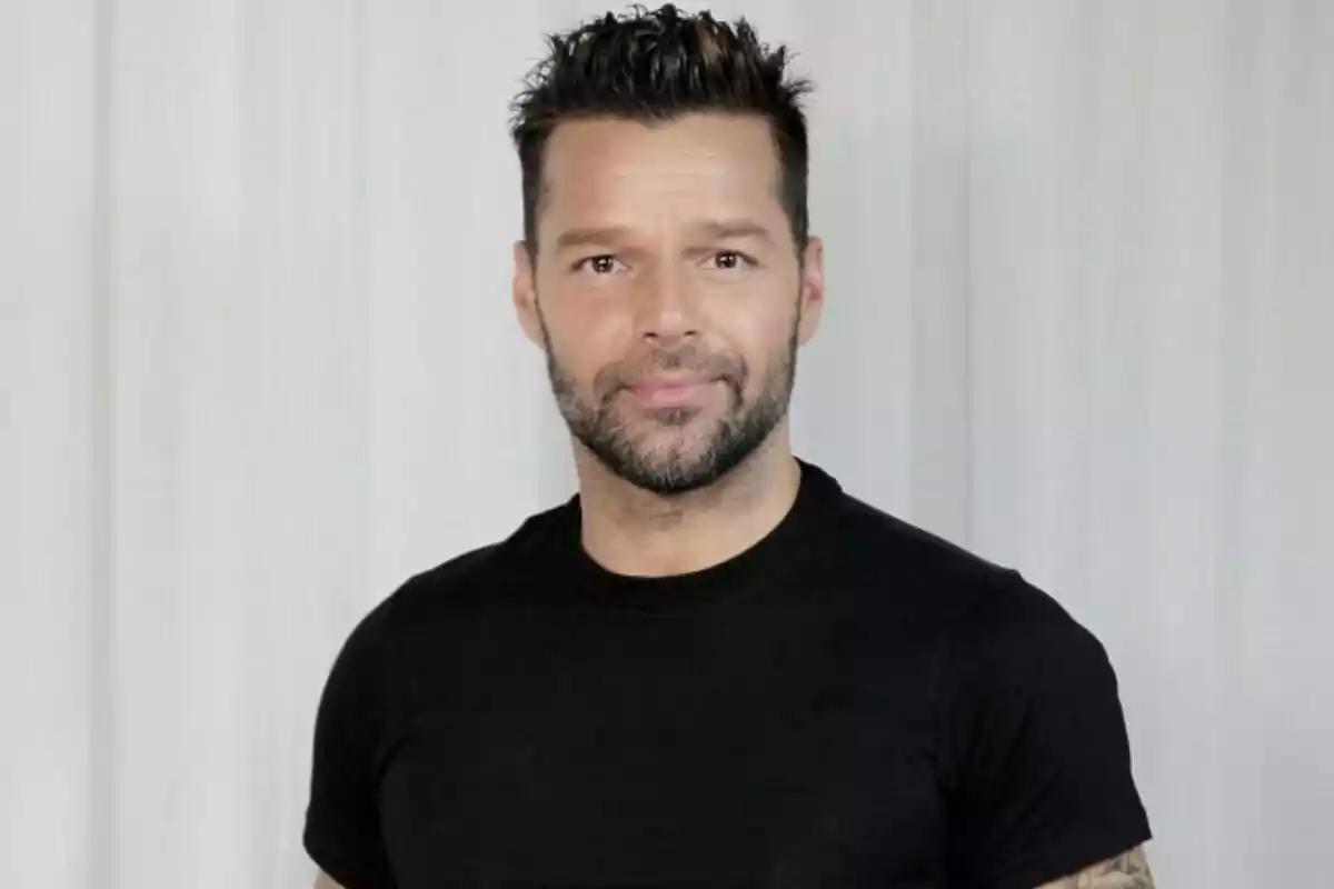 Ricky Martin vestido con camiseta negra, posando frente a una cortina blanca.