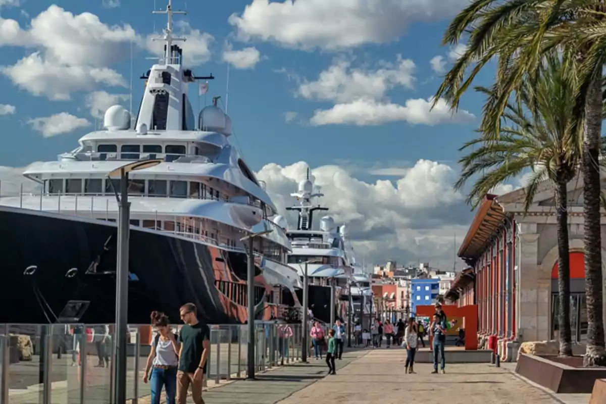 Yates de lujo atracados en un puerto con personas paseando por el muelle en un día soleado Yates de lujo atracados en un puerto con personas paseando por el muelle en un día soleado