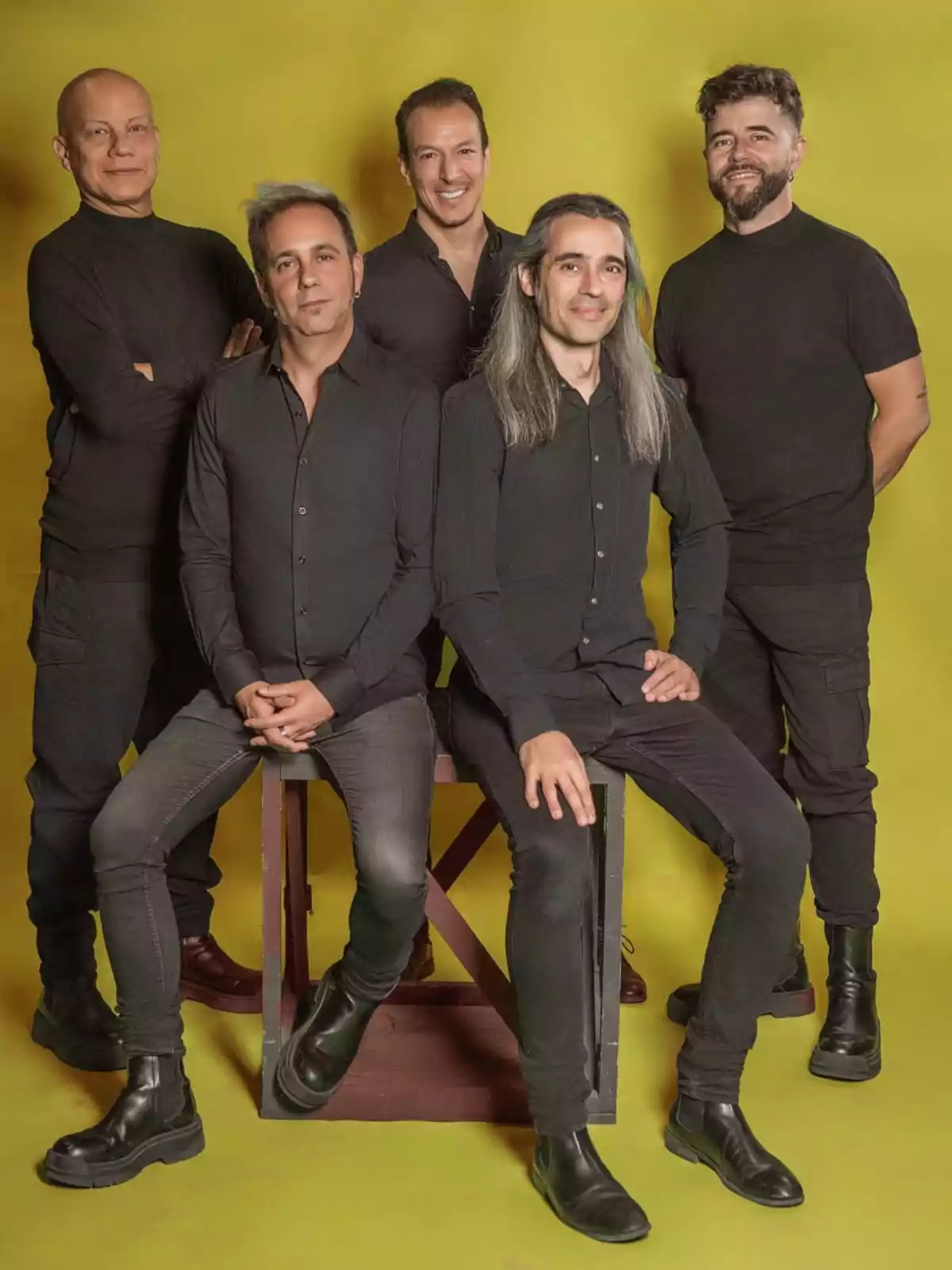 Un grupo de cinco personas vestidas de negro posando frente a un fondo amarillo.