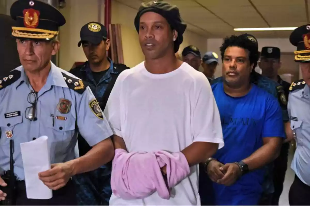 Un hombre escoltado por varios policías mientras lleva las manos cubiertas con una prenda rosa.