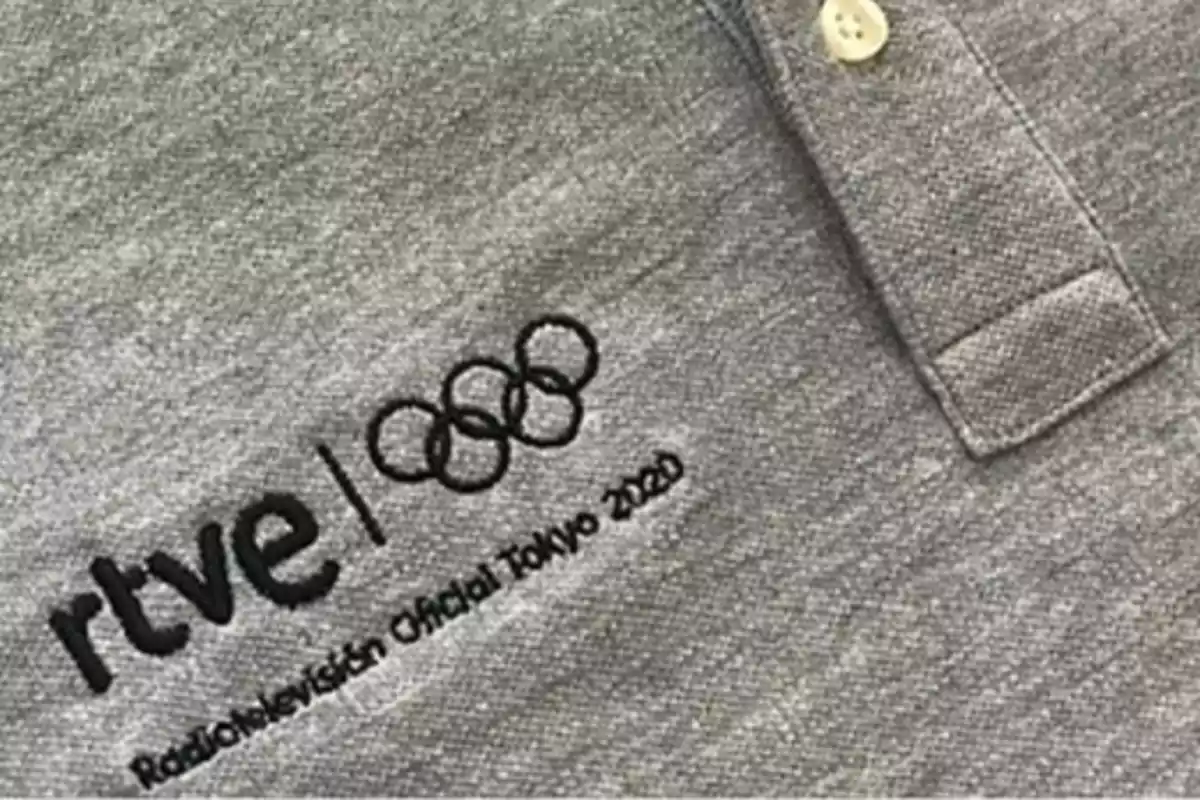 Camisa gris con el logo de RTVE y los anillos olímpicos, junto con el texto Camisa gris con el logo de RTVE y los anillos olímpicos, junto con el texto