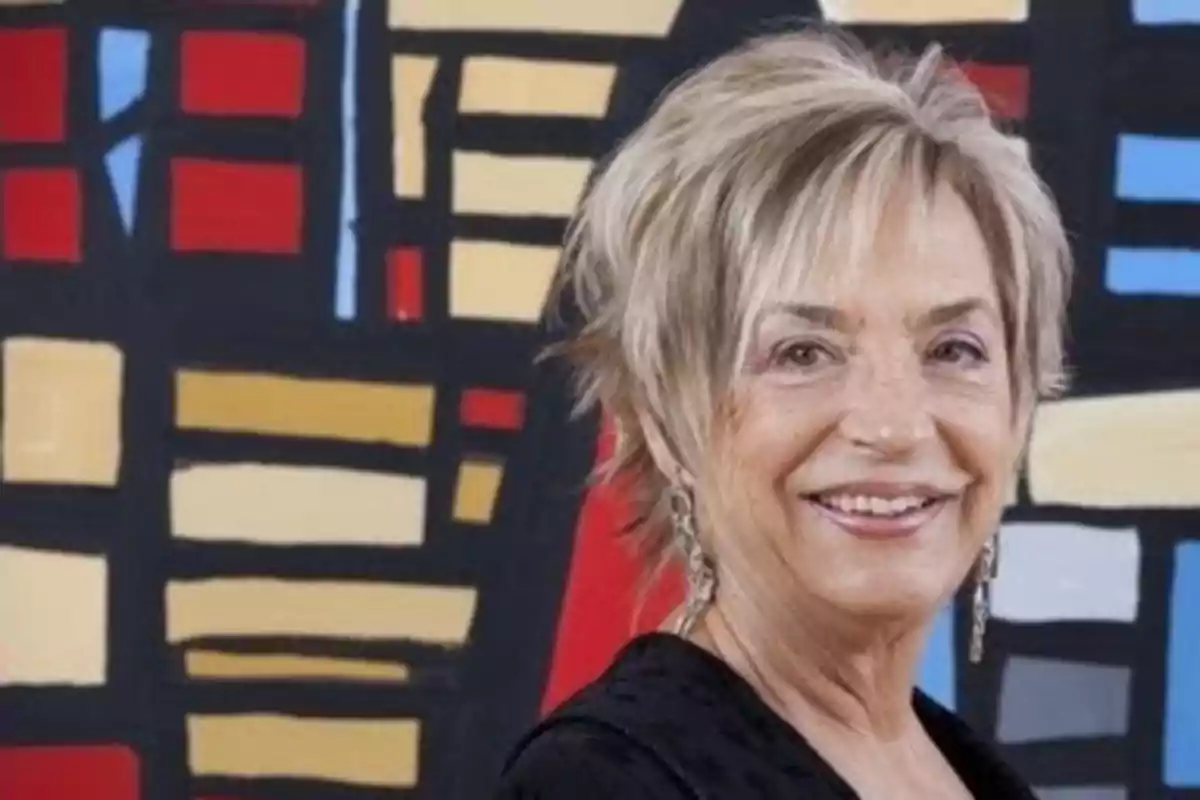 Una persona sonriente con cabello corto y rubio frente a un fondo colorido con formas geométricas. Una persona sonriente con cabello corto y rubio frente a un fondo colorido con formas geométricas.
