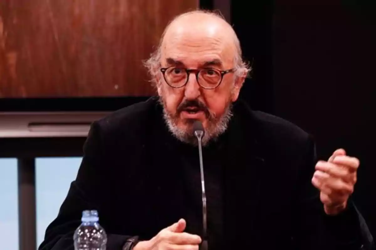 Un hombre con gafas y barba hablando en un micrófono durante una conferencia.