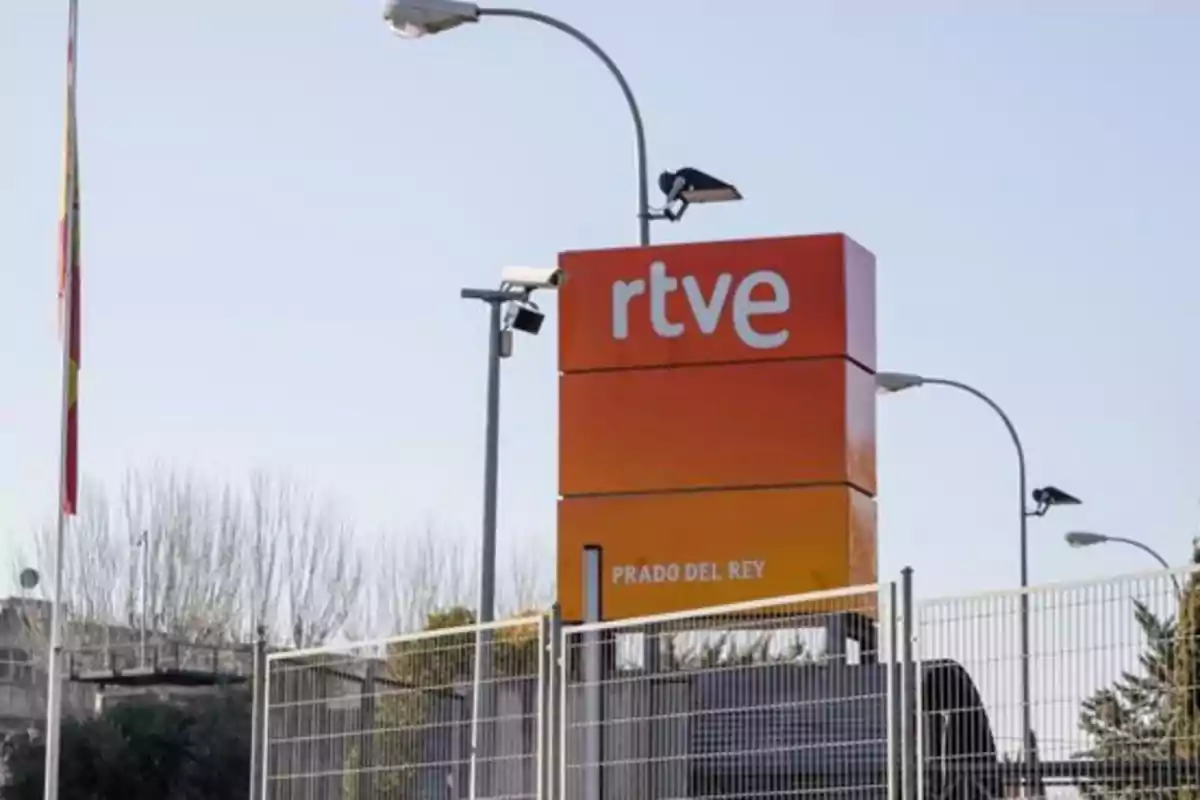 Entrada principal de RTVE en Prado del Rey con un cartel naranja y una bandera ondeando. Entrada principal de RTVE en Prado del Rey con un cartel naranja y una bandera ondeando.