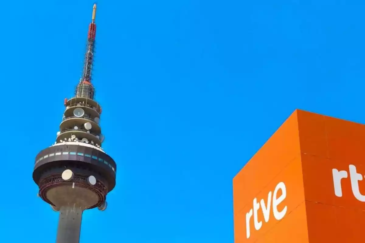 Torre de telecomunicaciones con un edificio naranja de RTVE en un día despejado.