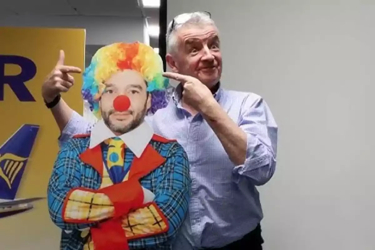 Hombre mayor sonriente señalando con ambas manos a una figura de cartón con cara de persona y disfraz de payaso con peluca de colores y nariz roja Hombre mayor sonriente señalando con ambas manos a una figura de cartón con cara de persona y disfraz de payaso con peluca de colores y nariz roja