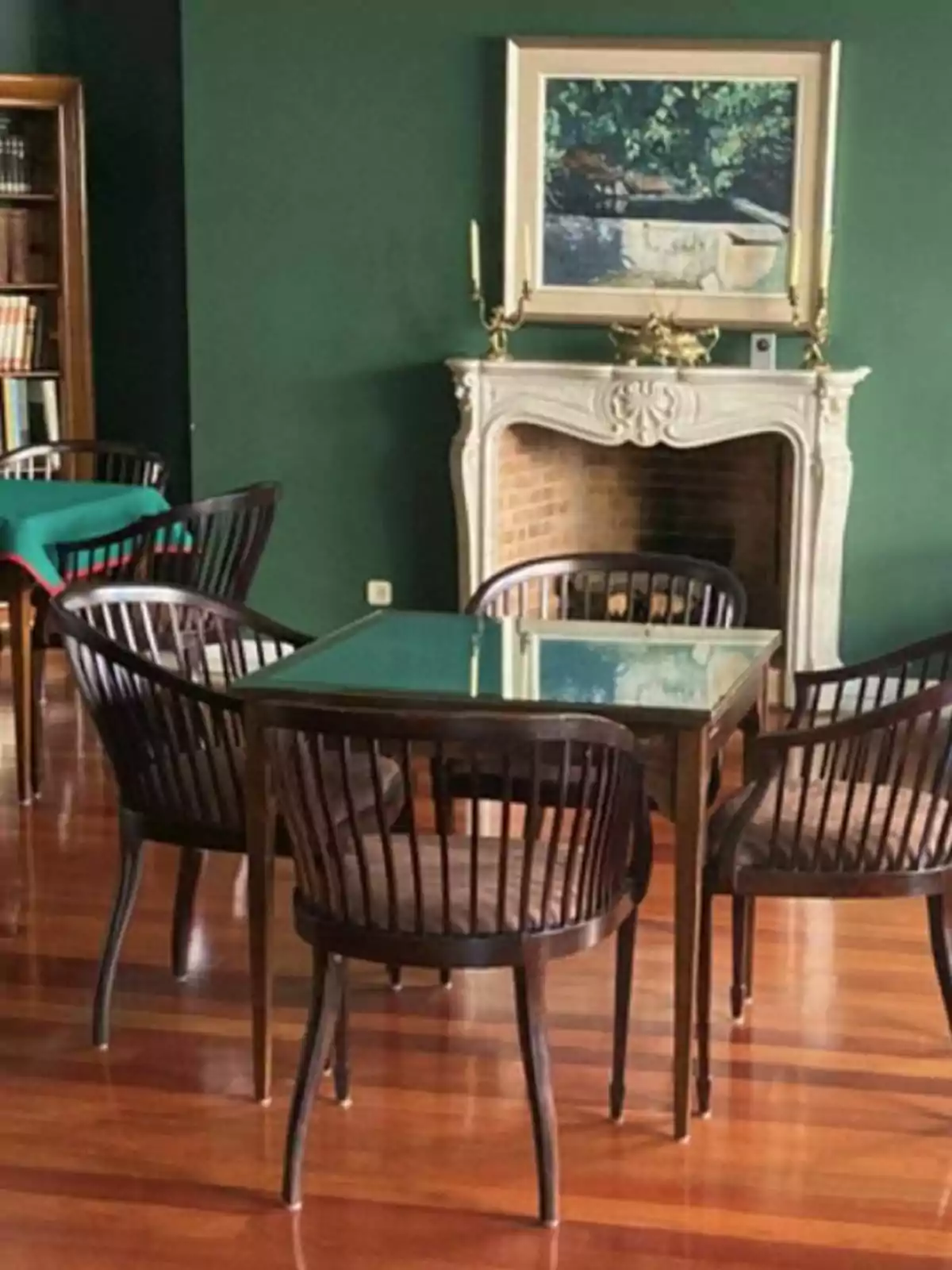 Sala con chimenea, mesa de cristal, sillas de madera y paredes verdes.