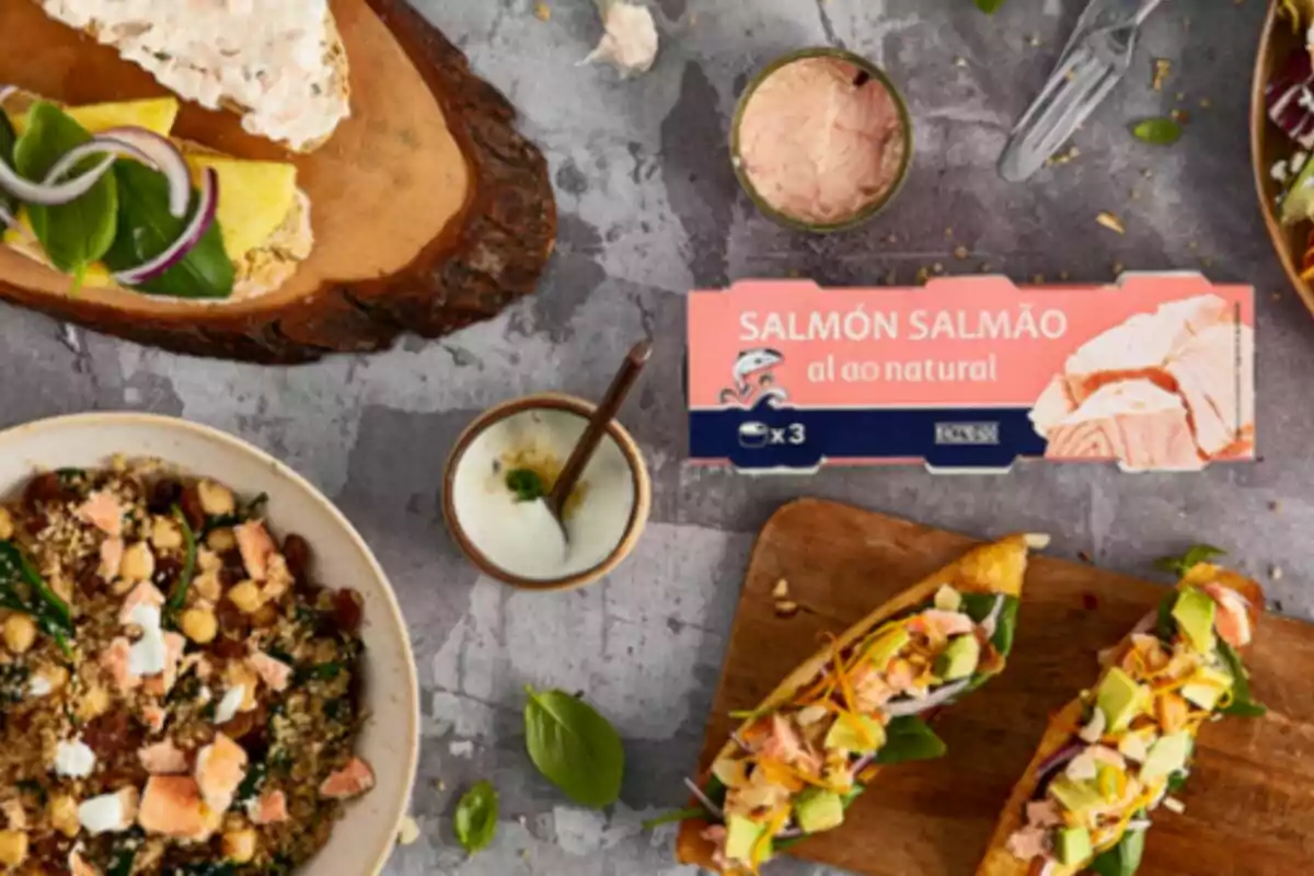 Una variedad de platos gourmet con salmón al natural de Mercadona en el centro; incluyendo ensaladas, tostadas y un dip, presentados sobre una mesa de piedra. Una variedad de platos gourmet con salmón al natural de Mercadona en el centro; incluyendo ensaladas, tostadas y un dip, presentados sobre una mesa de piedra.
