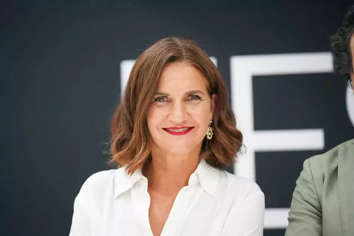 Samantha Vallejo-Nágera sonriendo con cabello castaño y blusa blanca frente a un fondo oscuro.