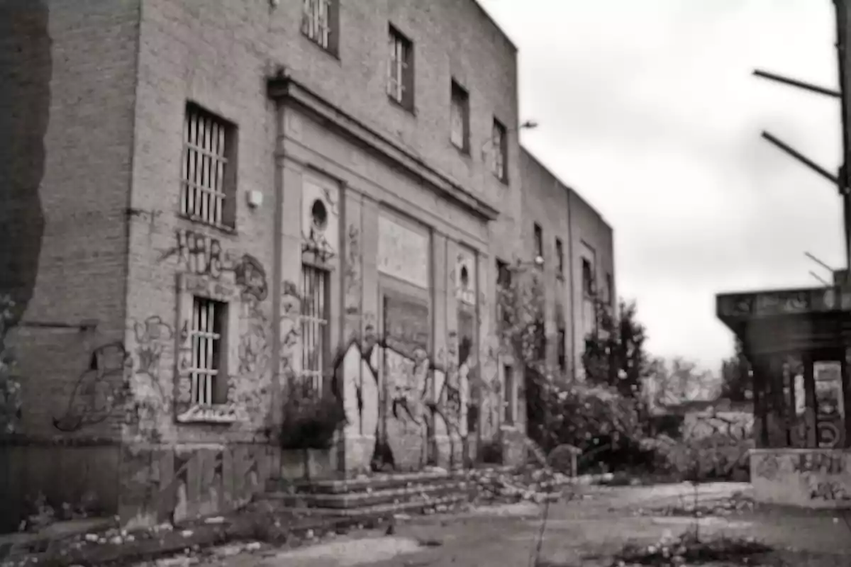 Edificio abandonado con grafitis en las paredes y vegetación creciendo alrededor.