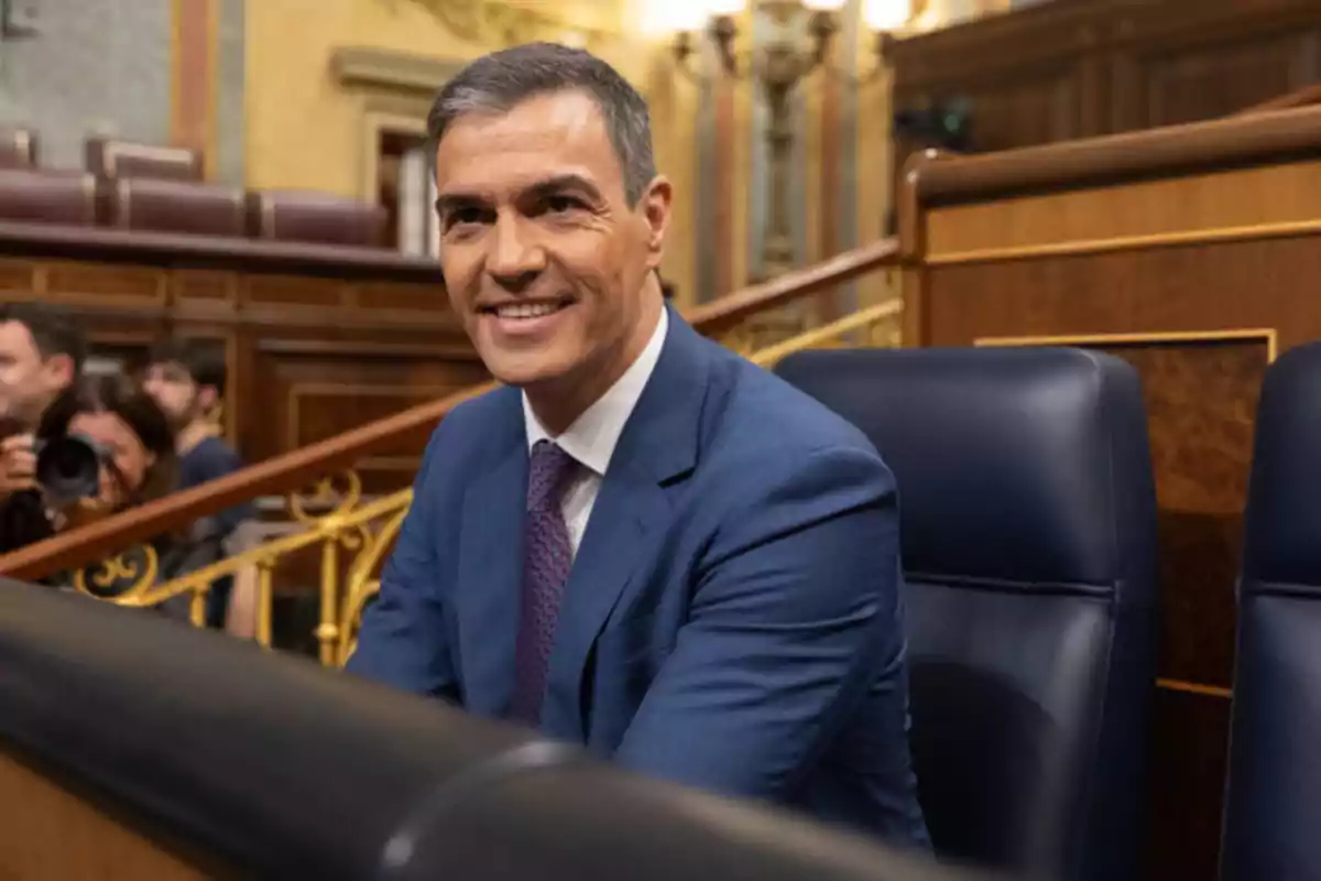 Hombre con traje azul sonriendo en un entorno parlamentario.