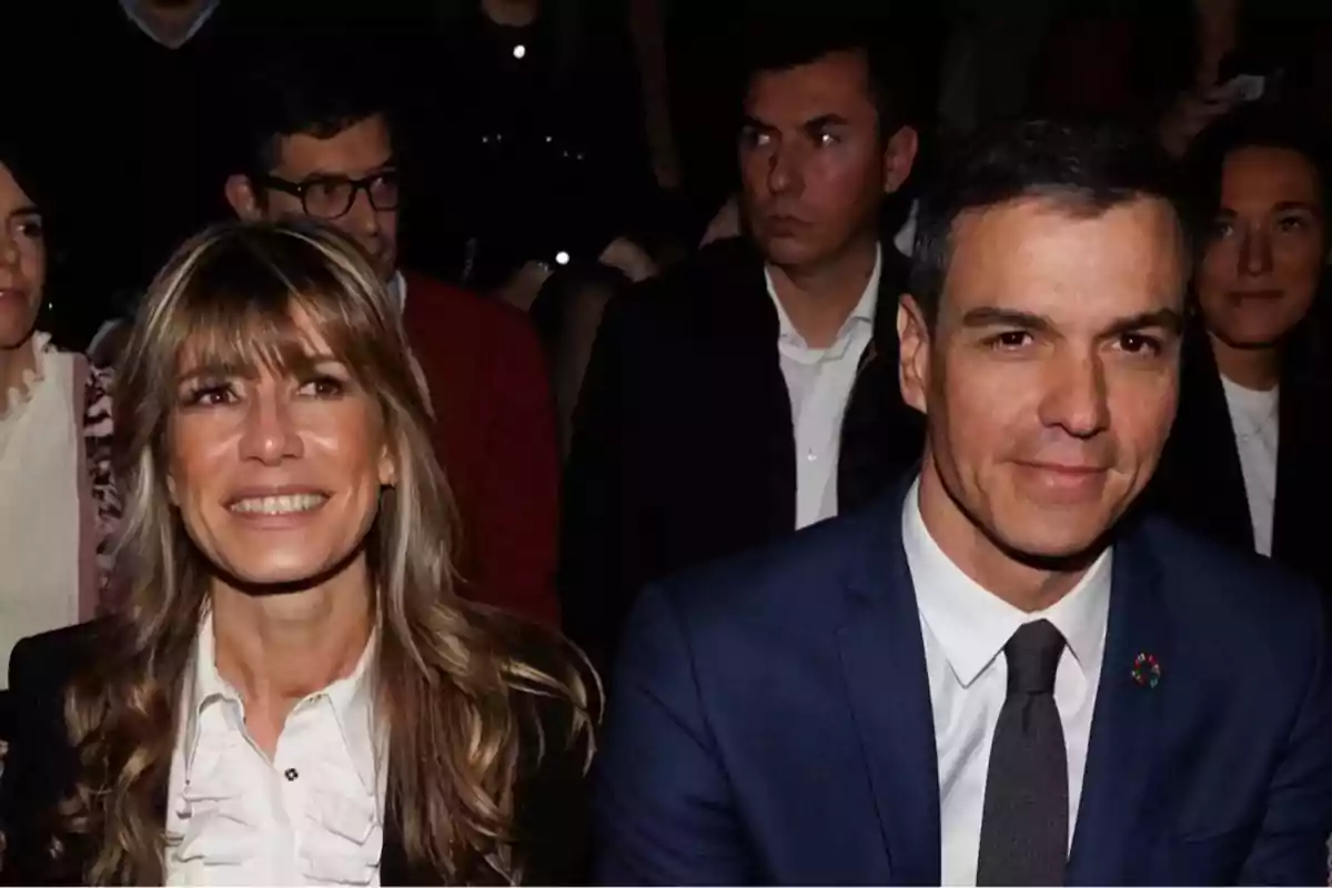 Una pareja sonriente en un evento formal, rodeada de otras personas.