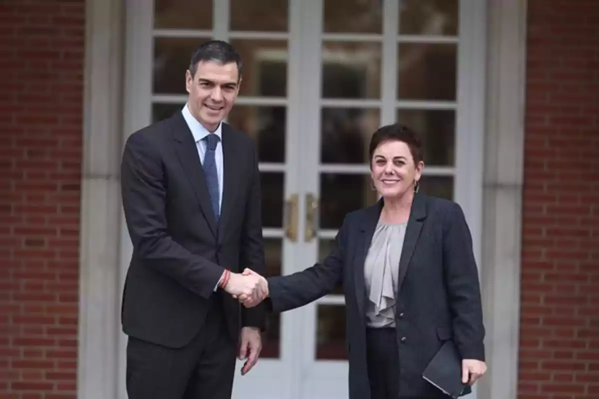 Dos personas dándose la mano frente a una puerta de vidrio.