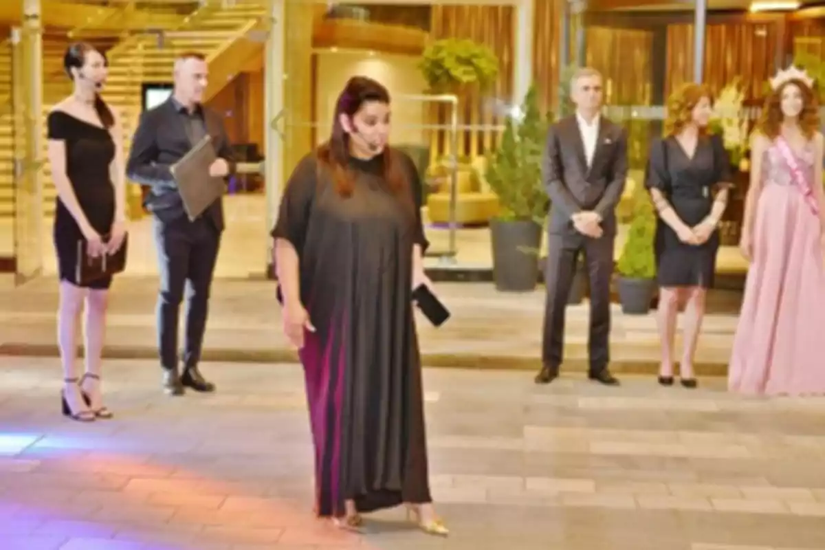 Un grupo de personas elegantemente vestidas se encuentra de pie en un evento en un lugar con decoración moderna y plantas.