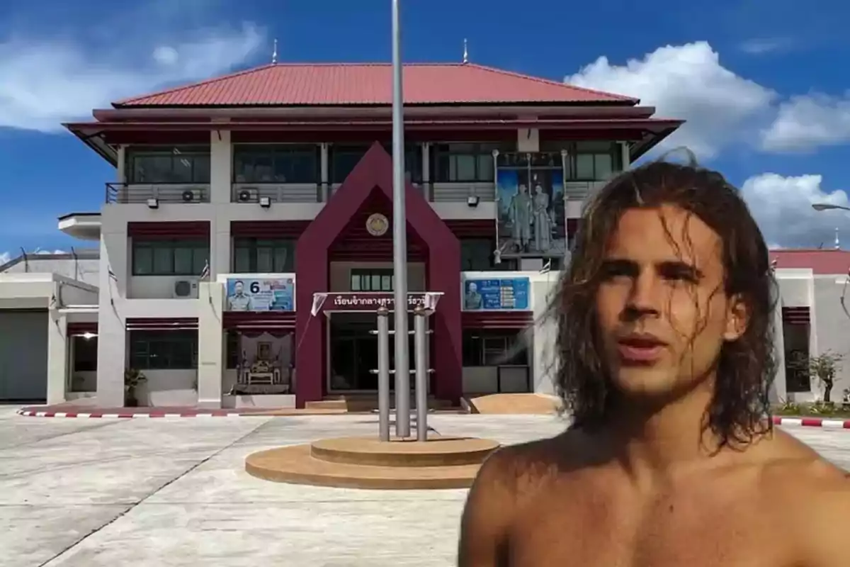 Un hombre sin camisa frente a un edificio con techo rojo y cielo azul.