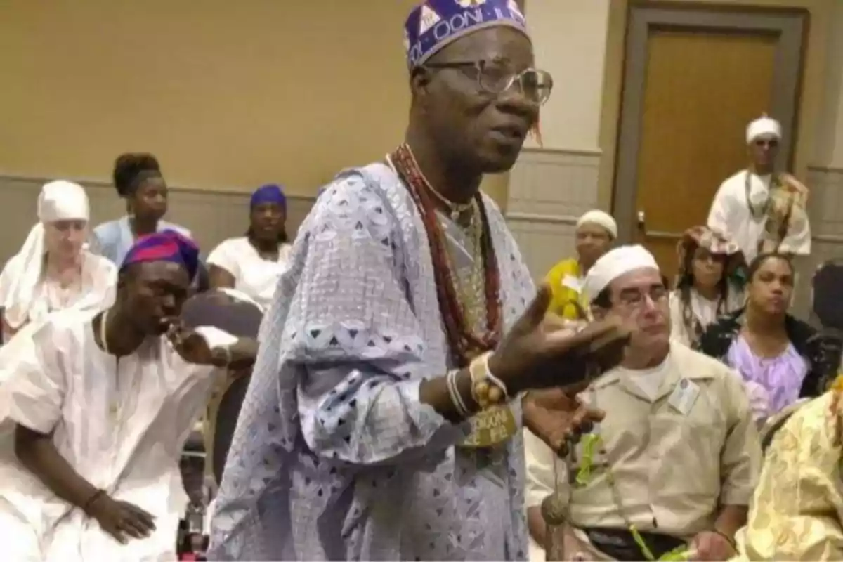 Un hombre vestido con ropa tradicional africana habla frente a un grupo de personas que también llevan vestimenta cultural.