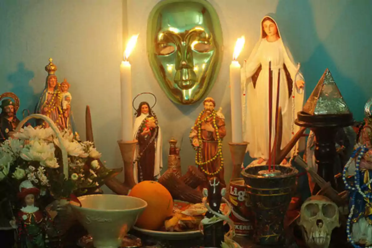 Un altar con estatuillas religiosas, velas encendidas, una máscara verde, flores y ofrendas.