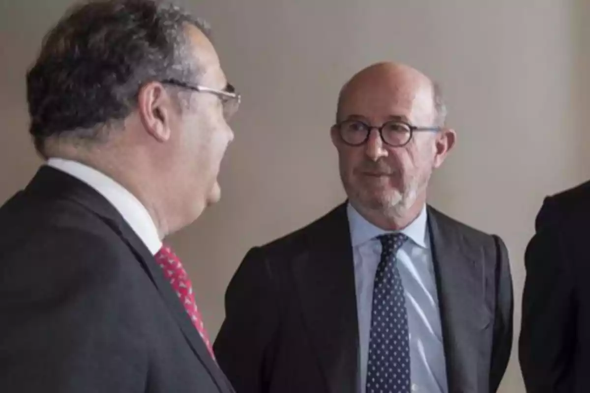 Dos hombres de traje conversan en un ambiente formal. Dos hombres de traje conversan en un ambiente formal.