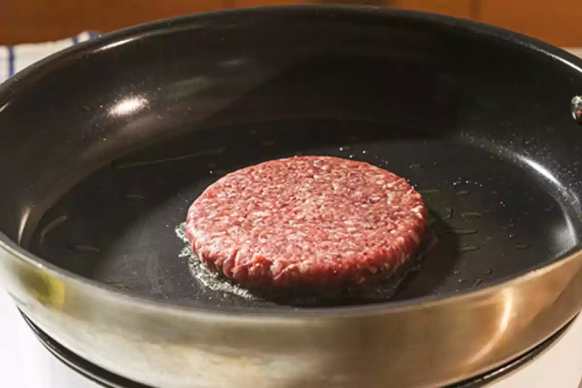 Hamburguesa cruda cocinándose en un sartén con un poco de aceite Hamburguesa cruda cocinándose en un sartén con un poco de aceite