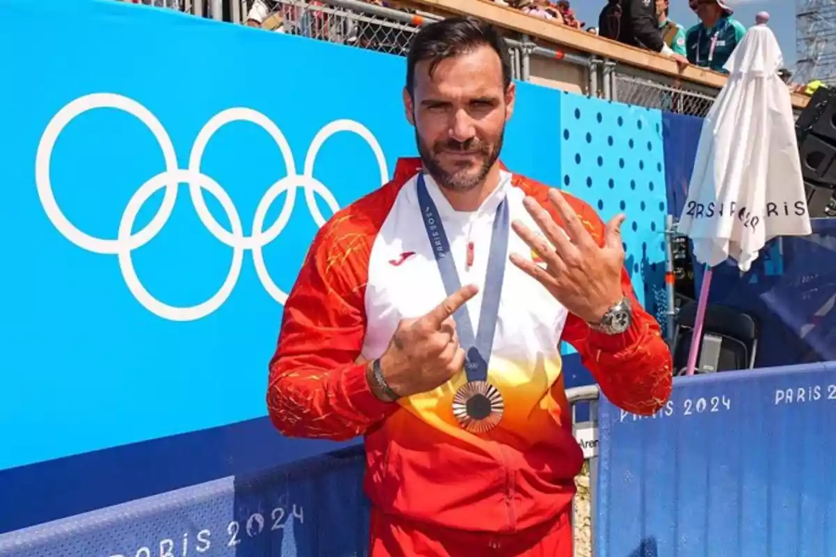 Un atleta con medalla y uniforme rojo y blanco posa frente a un cartel de los Juegos Olímpicos de París 2024.