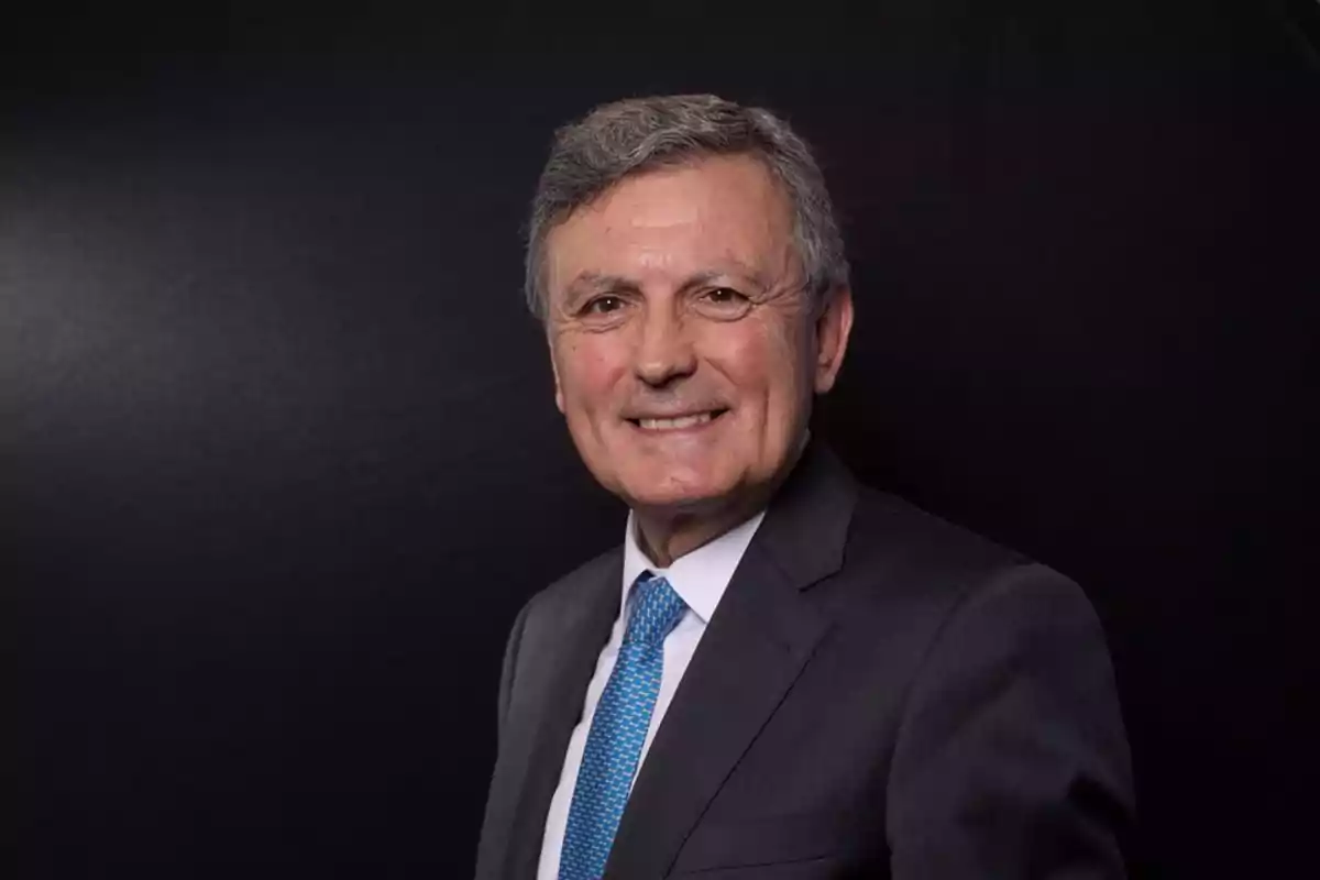 Hombre mayor sonriendo con traje oscuro y corbata azul sobre un fondo negro. Hombre mayor sonriendo con traje oscuro y corbata azul sobre un fondo negro.