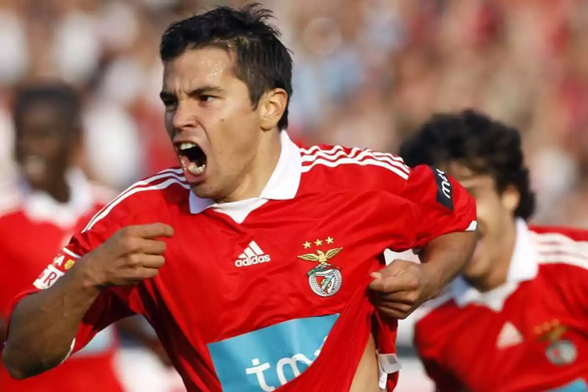 Futbolista celebrando un gol con pasión mientras sostiene la camiseta del Benfica Futbolista celebrando un gol con pasión mientras sostiene la camiseta del Benfica