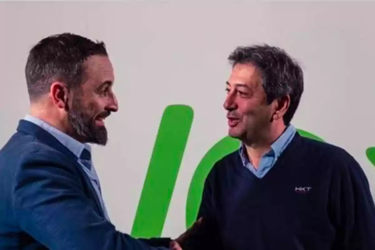 Dos hombres estrechándose la mano y sonriendo frente a un fondo con letras verdes.