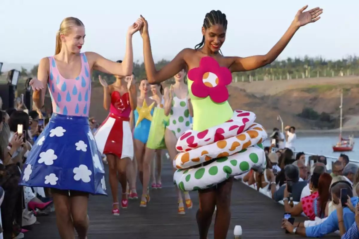 Desfile de moda al aire libre con modelos vistiendo trajes coloridos y temáticos mientras caminan por una pasarela rodeada de espectadores.