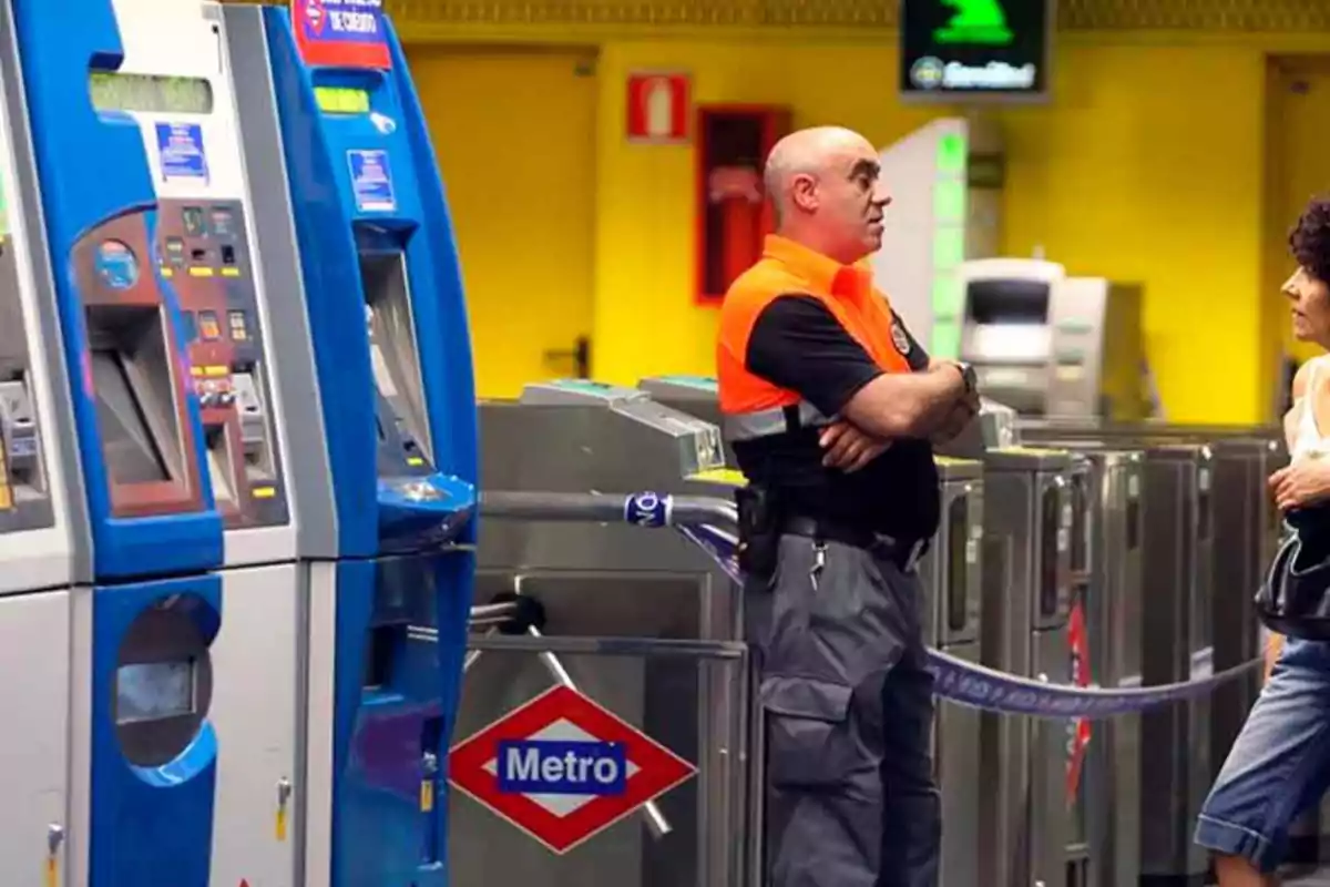 Un guardia de seguridad conversa con una mujer junto a las máquinas expendedoras de boletos y los torniquetes en una estación de metro